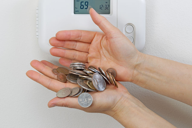 hands holding change in front of a thermostat in a home.