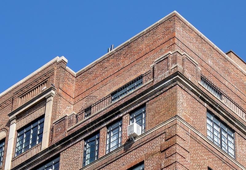 A upper exterior corner of a multi-story brick building set against a clear blue sky.