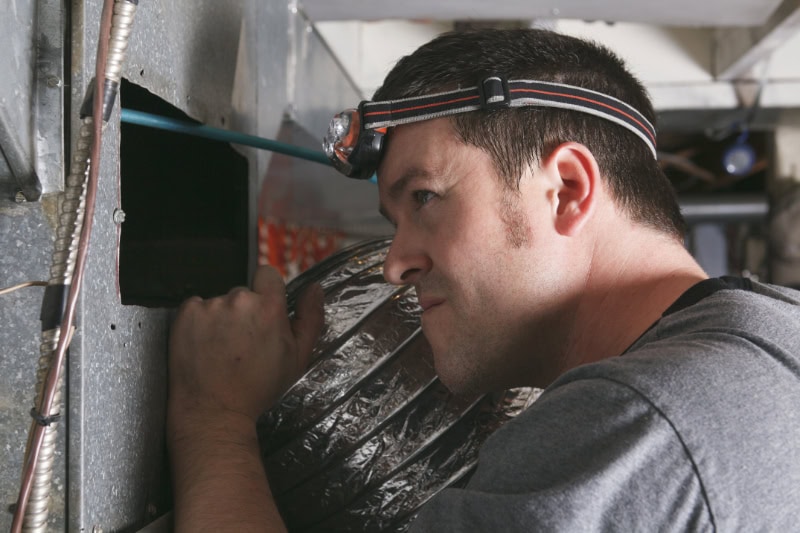 Why Is My Furnace Leaking Water? Photo of a maintenance working inspecting an air vent.