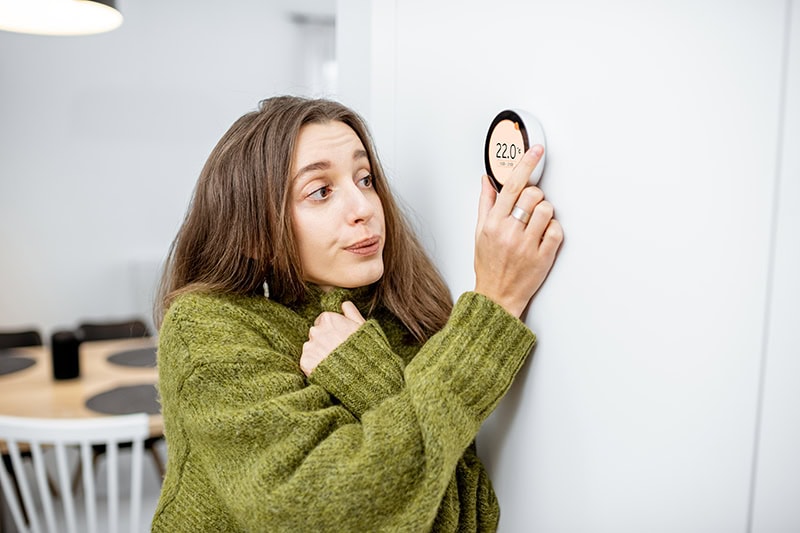 woman shivering in a sweater as she adjusts her thermostat.