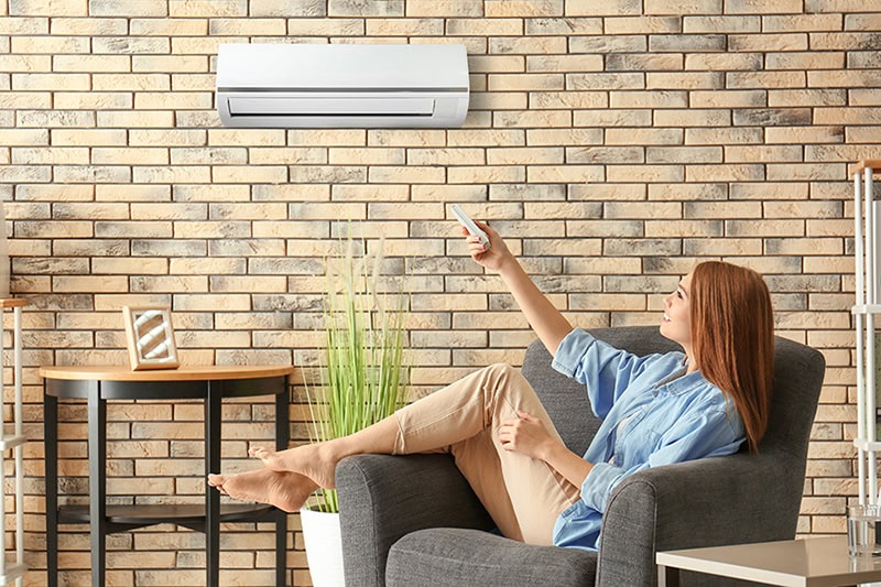Install a Mini Split in Your Michigan Home for Zoned Cooling. Photo of a young woman switching on air conditioning while sitting in an armchair.